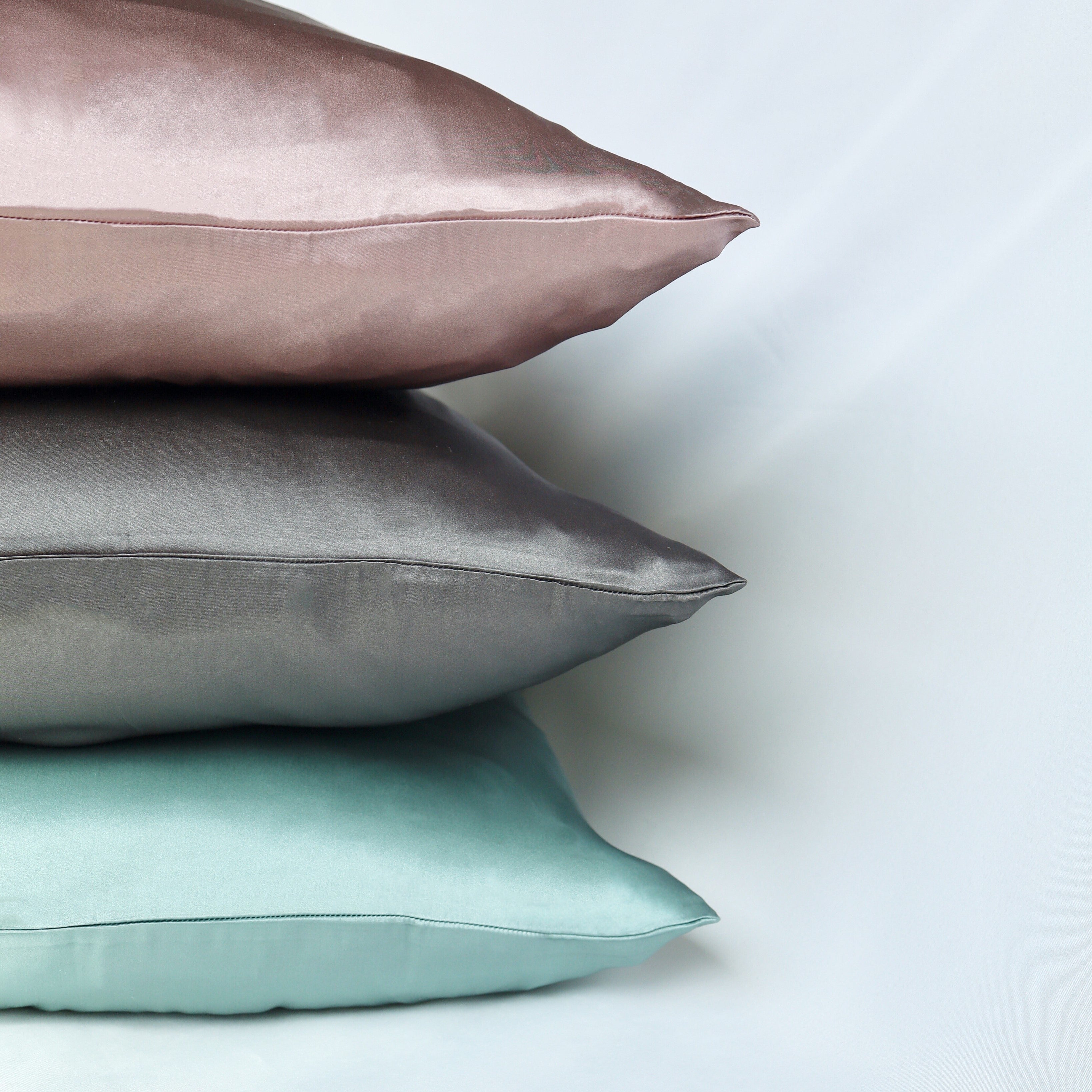 Three Paradise Pillowcase silk pillows in pink, gray, and green on a light background