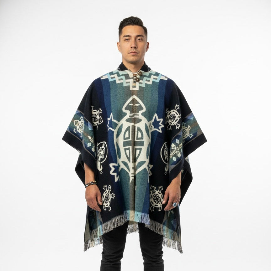 A man modeling a dark navy blue and teal poncho with white geometric and turtle designs, set against a plain white studio background.