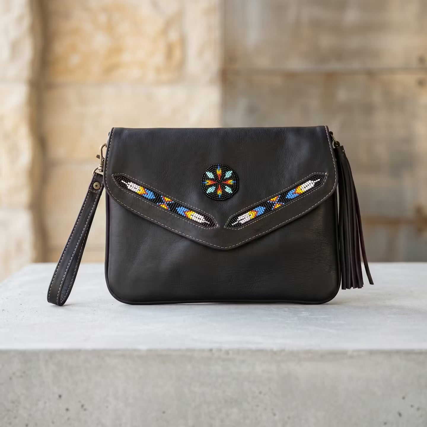 Black handbag with colorful embroidery and tassels on a stone surface.