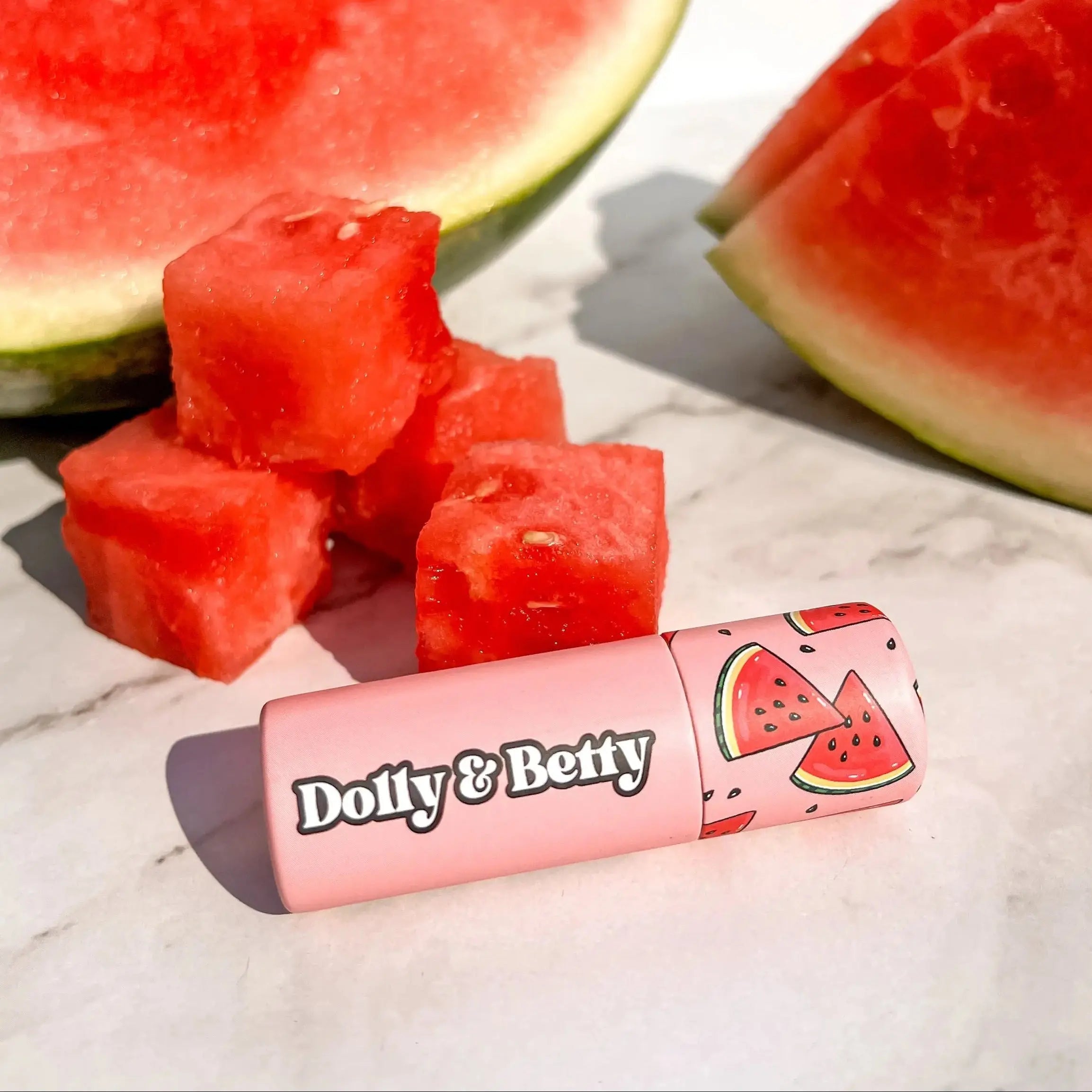 Pink lip balm with watermelon design and watermelon slices on a marble surface