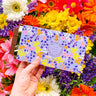 Earl Grey milk chocolate bar with floral packaging held against a colorful flower backdrop.