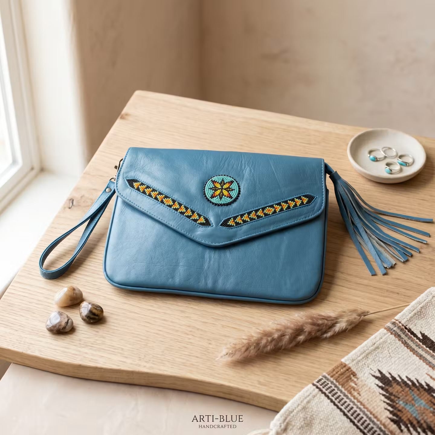 OldTribes Blue handbag with tassel on a wooden surface, surrounded by decorative items.