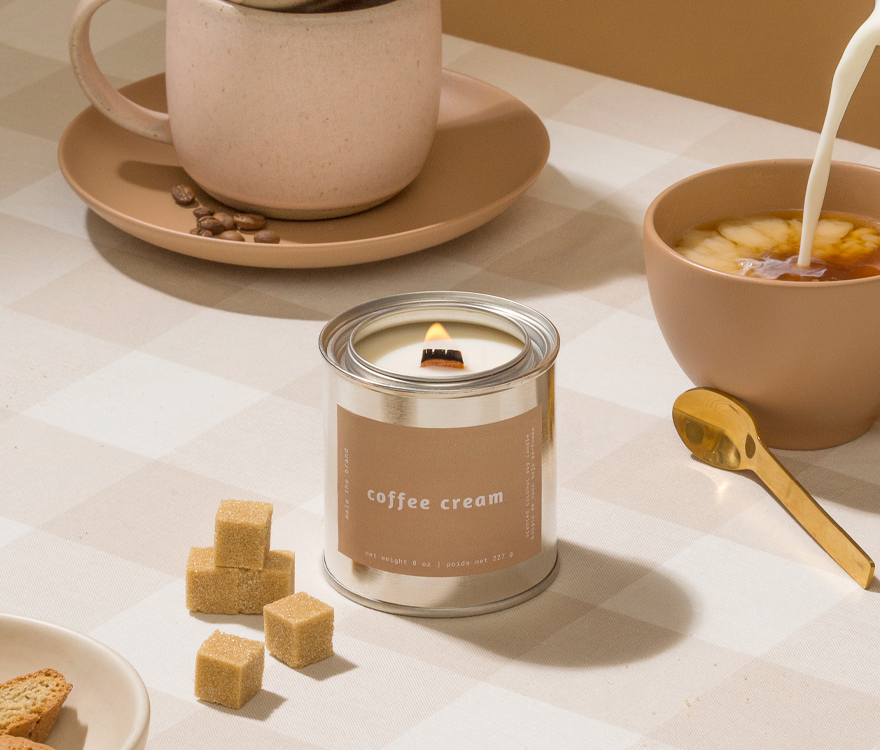 Candle labeled 'coffee cream' with a coffee cup and bowl in the background on a light surface.