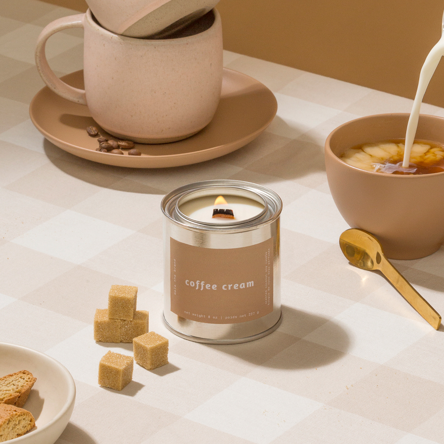 Candle labeled 'coffee cream' with a coffee cup and bowl in the background on a light surface.