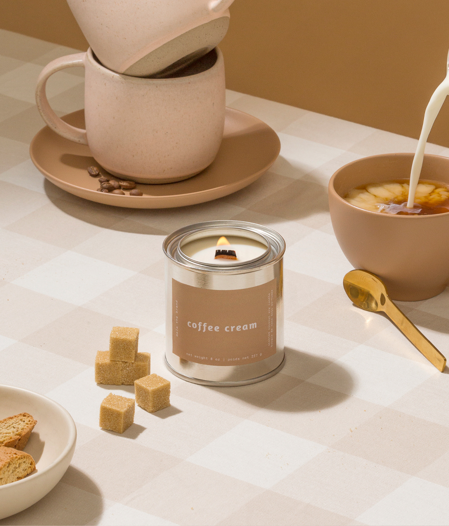 Candle labeled 'coffee cream' with a coffee cup and bowl in the background on a light surface.