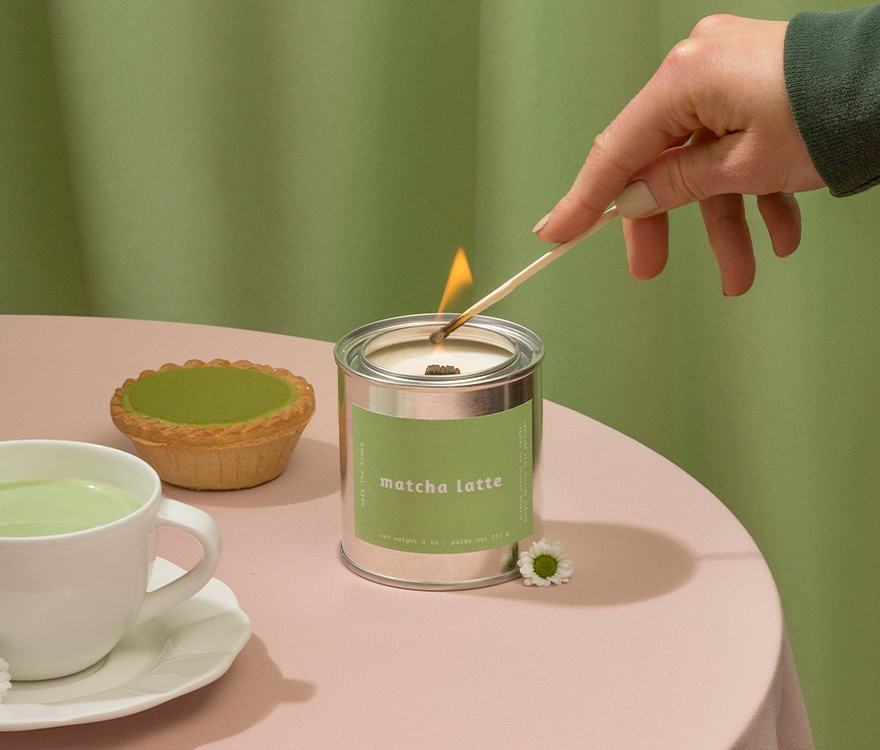 Person lighting a matcha latte candle with a cup of matcha and a small pie on a table.
