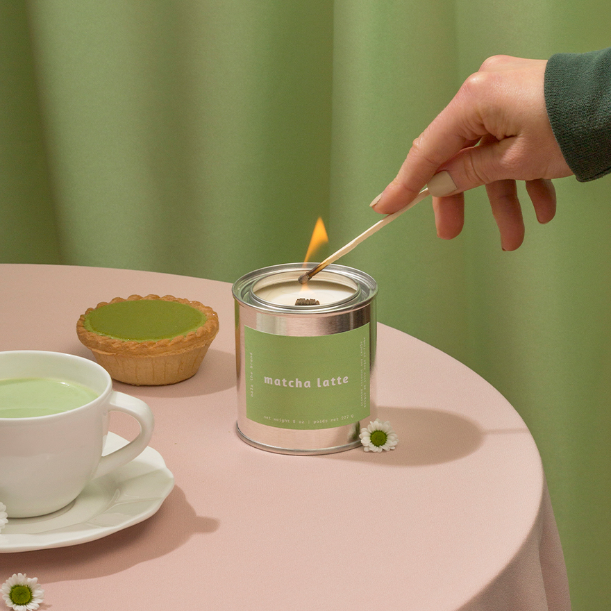 Person lighting a matcha latte candle with a cup of matcha and a small pie on a table.
