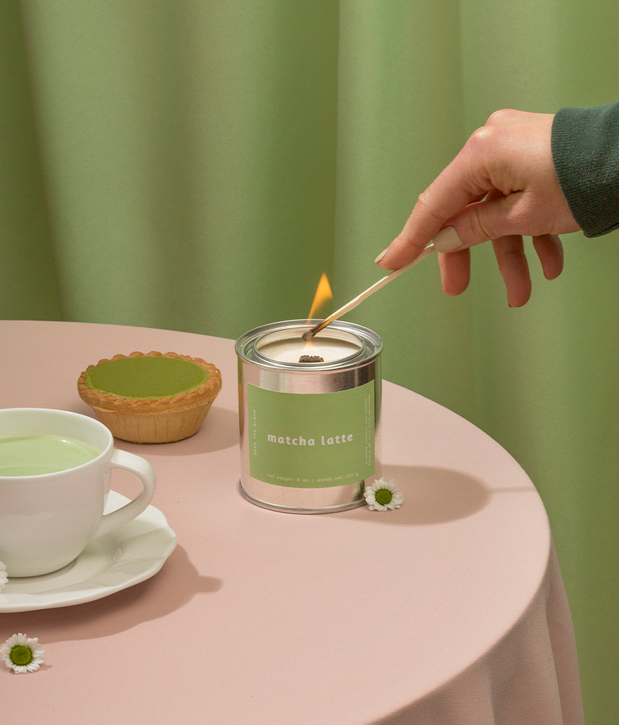 Person lighting a matcha latte candle with a cup of matcha and a small pie on a table.