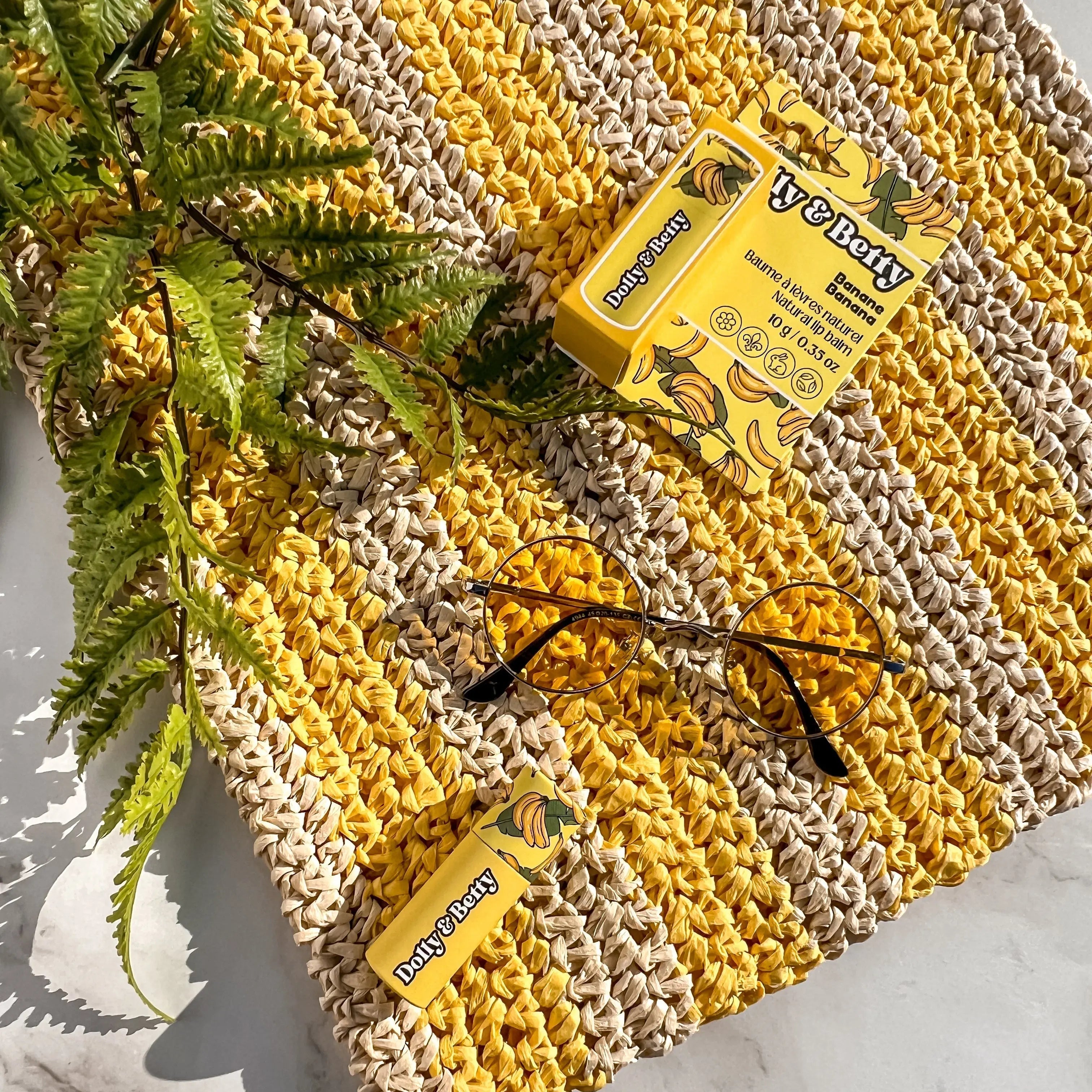 Yellow and beige textured mat with a box of Poby Betty cookies, glasses, and green leaves on a marble surface.