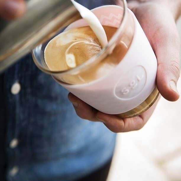 Person holding a 12OZ Perfect Pink Glass Travel Tumbler with coffee, showcasing SOL Cups' eco-friendly design.