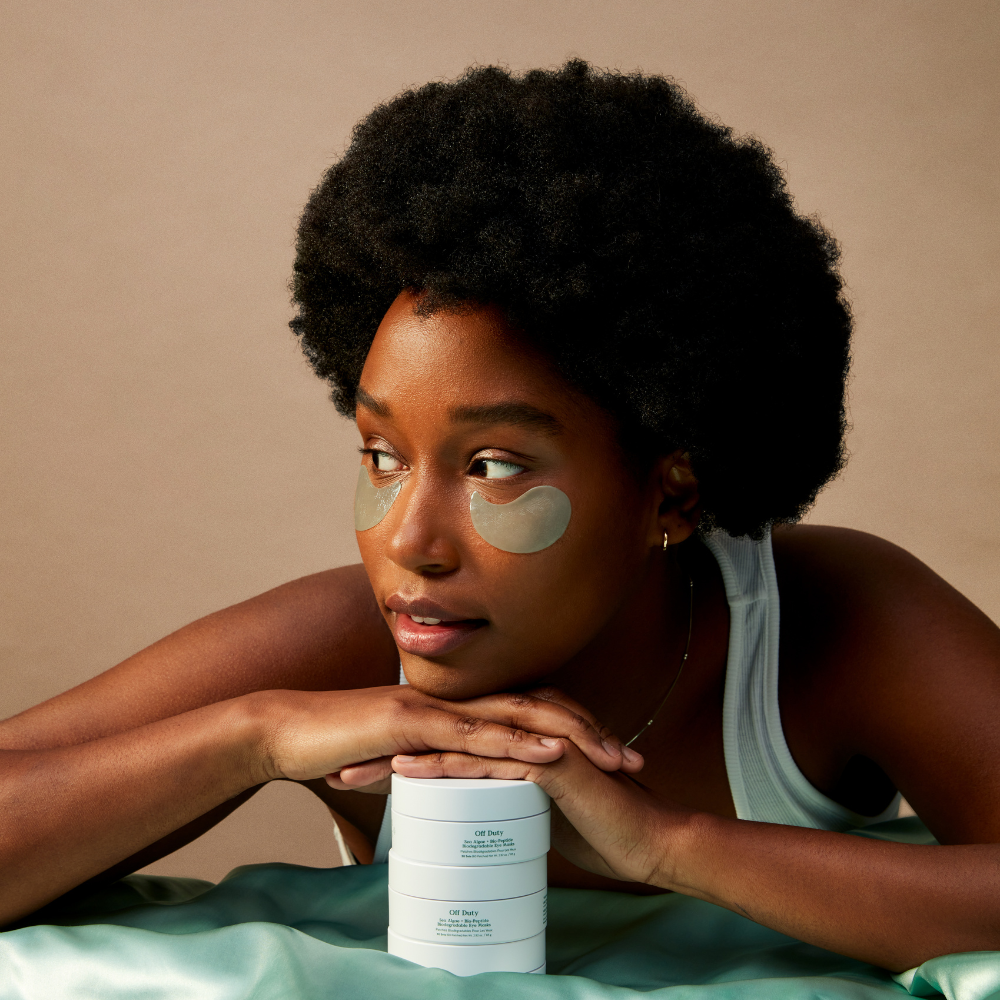 Model with biodegradable eye masks resting on a stack of skincare products, showcasing hydration and rejuvenation.