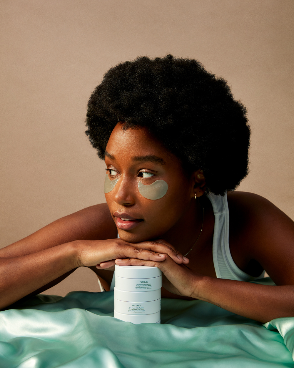 Model with biodegradable eye masks resting on a stack of skincare products, showcasing hydration and rejuvenation.