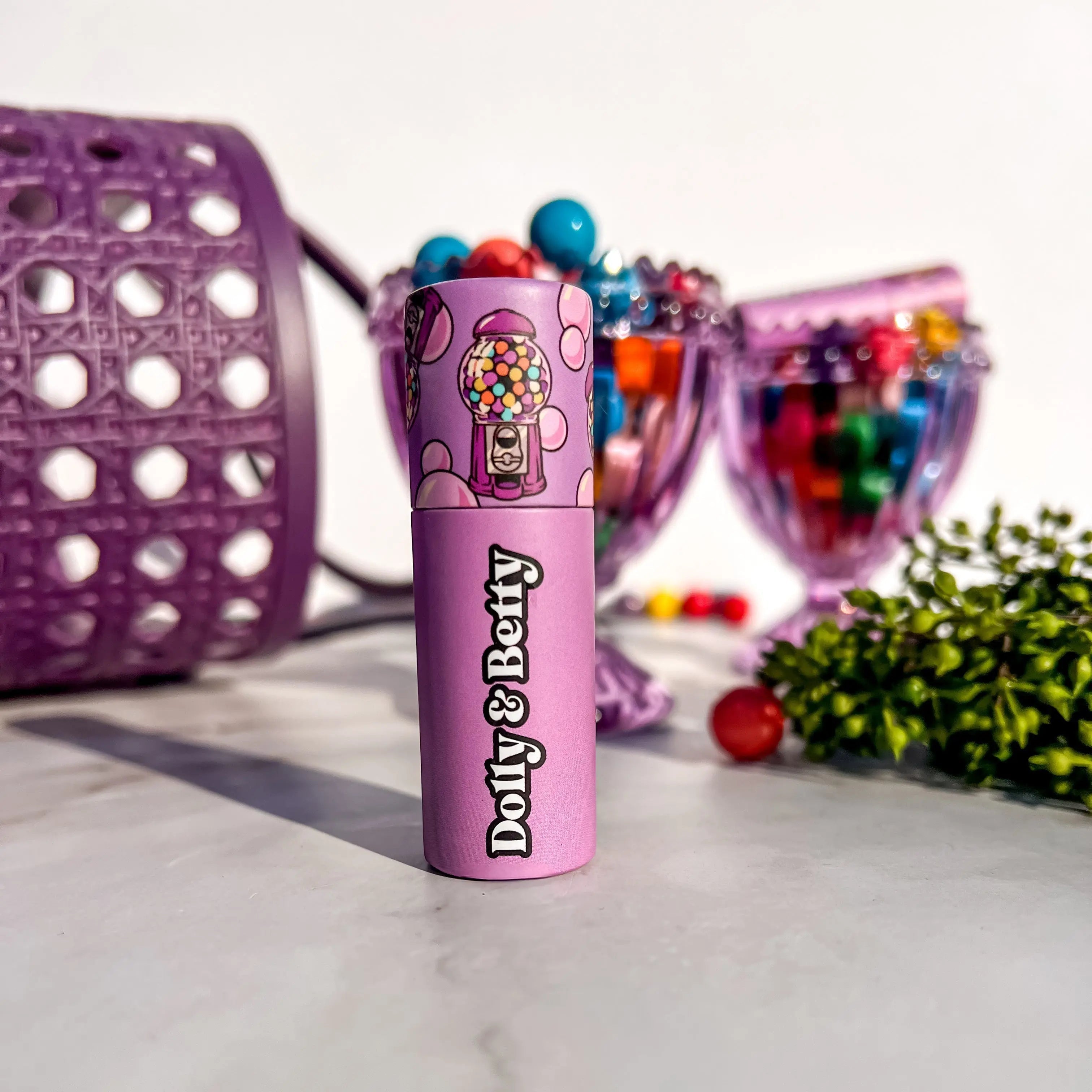 Pink lip balm with 'Dolly & Betty' branding in front of colorful candy display