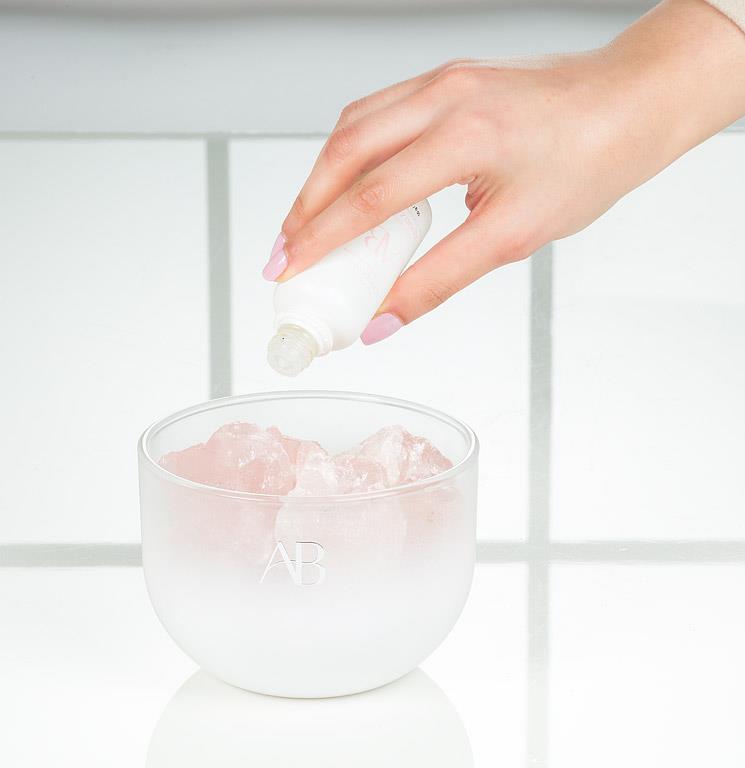 Hand applying AB rose quartz crystal room fragrance with a blurred background