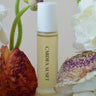 Skincare bottle labeled 'Cardea Auset' surrounded by flowers and leaves