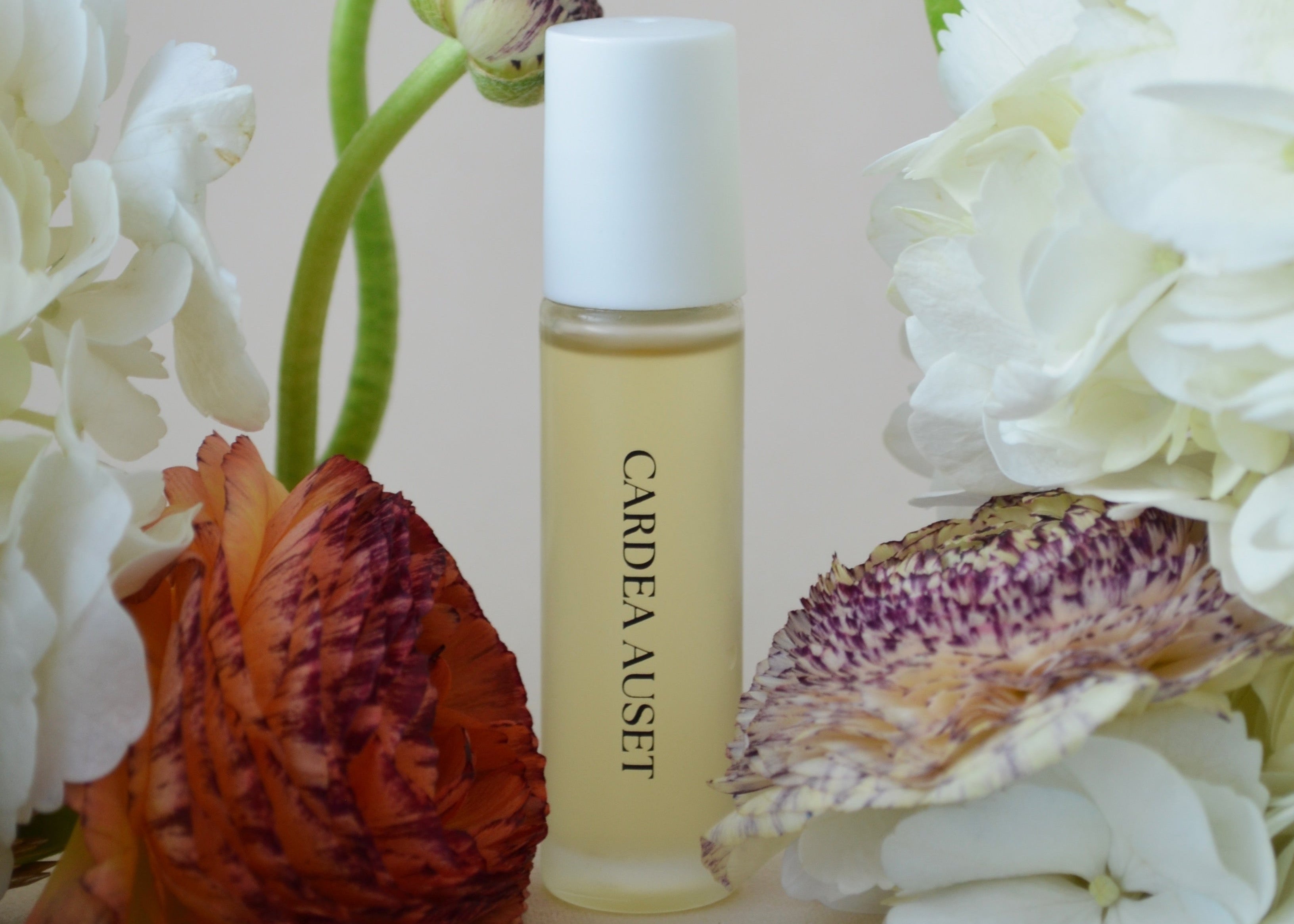 Skincare bottle labeled 'Cardea Auset' surrounded by flowers and leaves