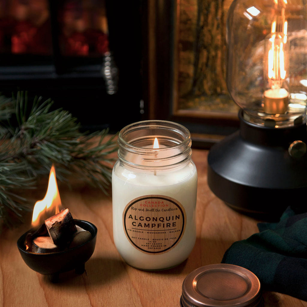 Candle with a label on a wooden surface next to a lantern and small candle from Stop and Smell the Candles