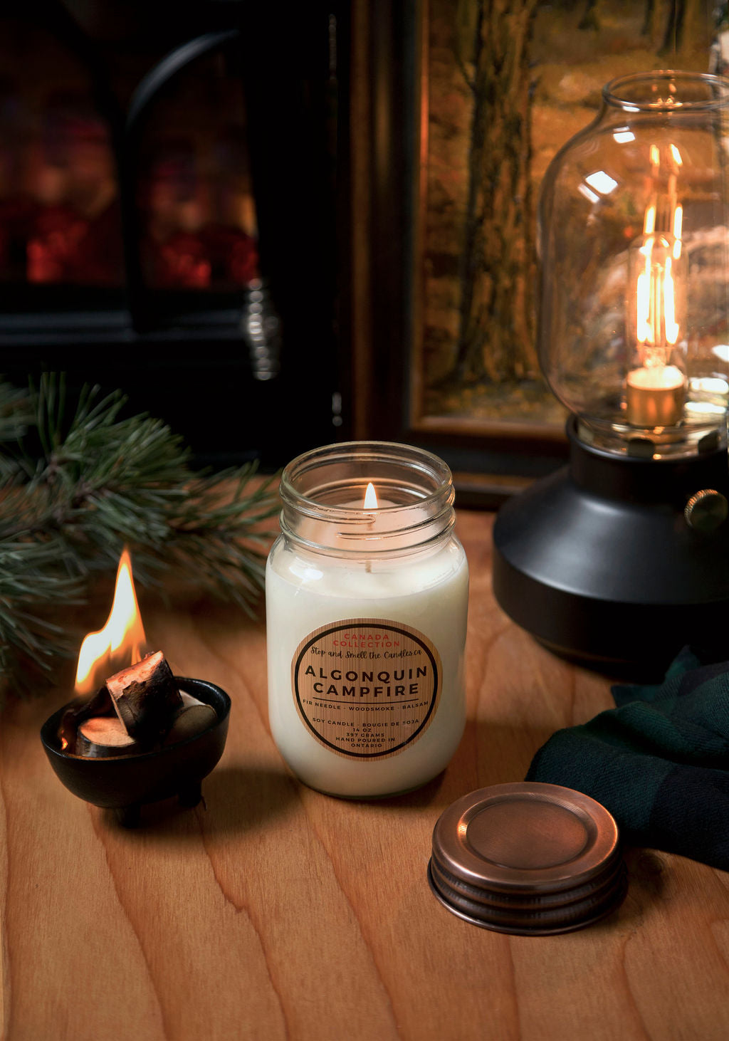 Candle with a label on a wooden surface next to a lantern and small candle from Stop and Smell the Candles