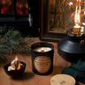 Stopandsmellthecandles Algonquin Campfire soy candle – 8 oz black jar with lit wooden wick and wooden lid beside pine branches