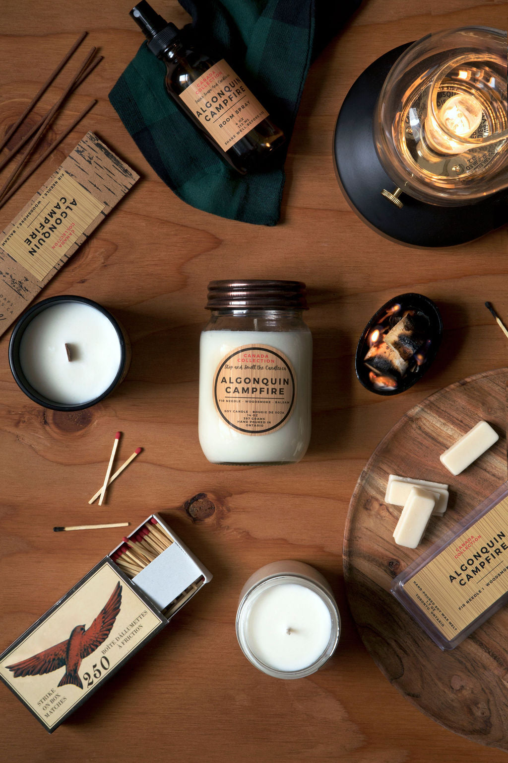 Collection of candles and matchbox on a wooden surface with 'Alconquin Campfire' branding.