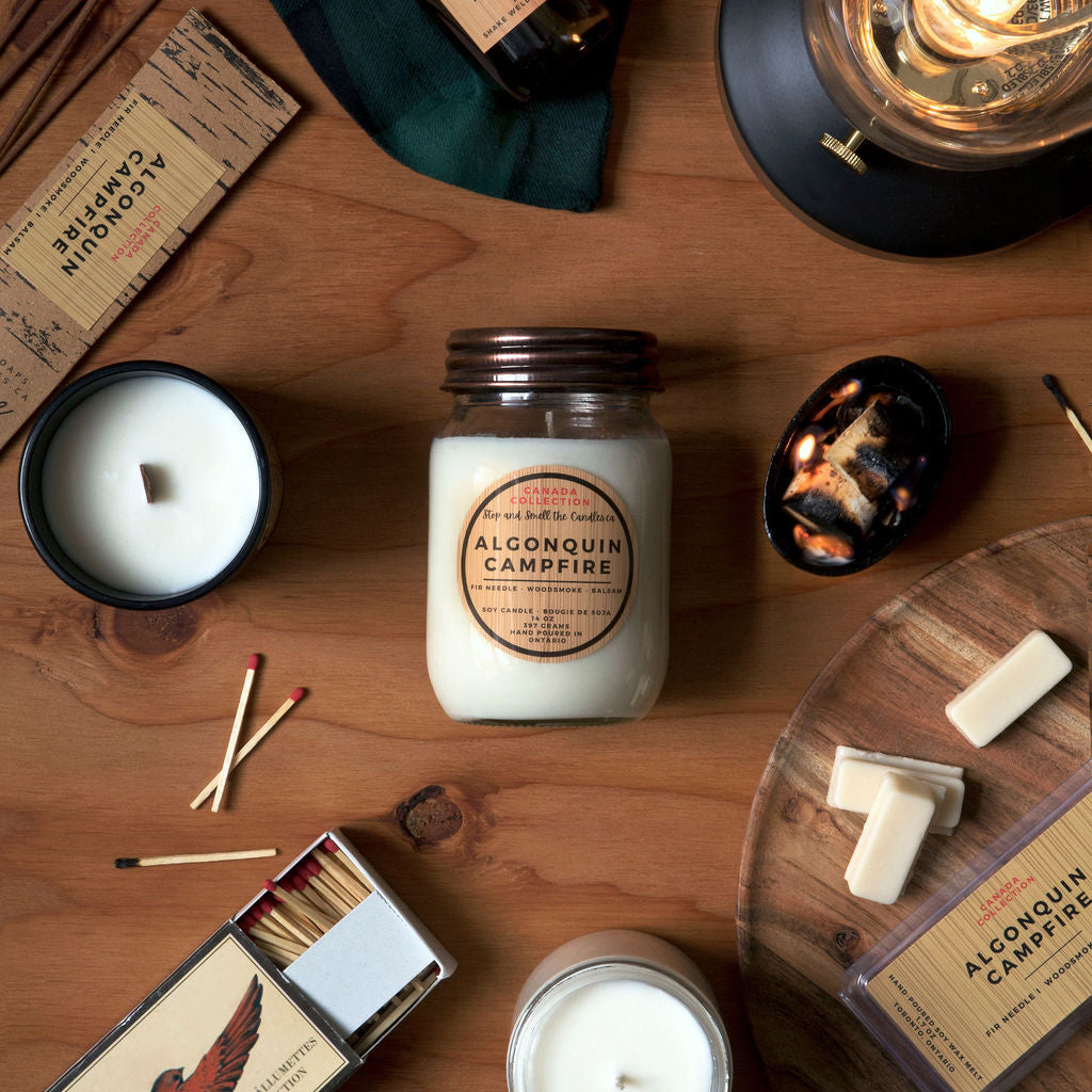 Collection of candles and matchbox on a wooden surface with 'Alconquin Campfire' branding from Stop and Smell the Candles