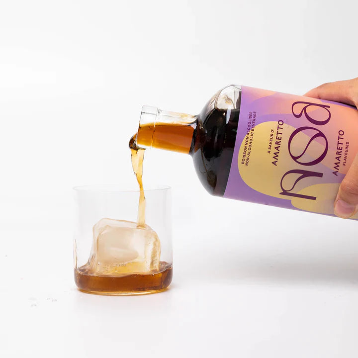 Bottle of NOSA Amaretto being poured into a glass with ice cubes on a white background