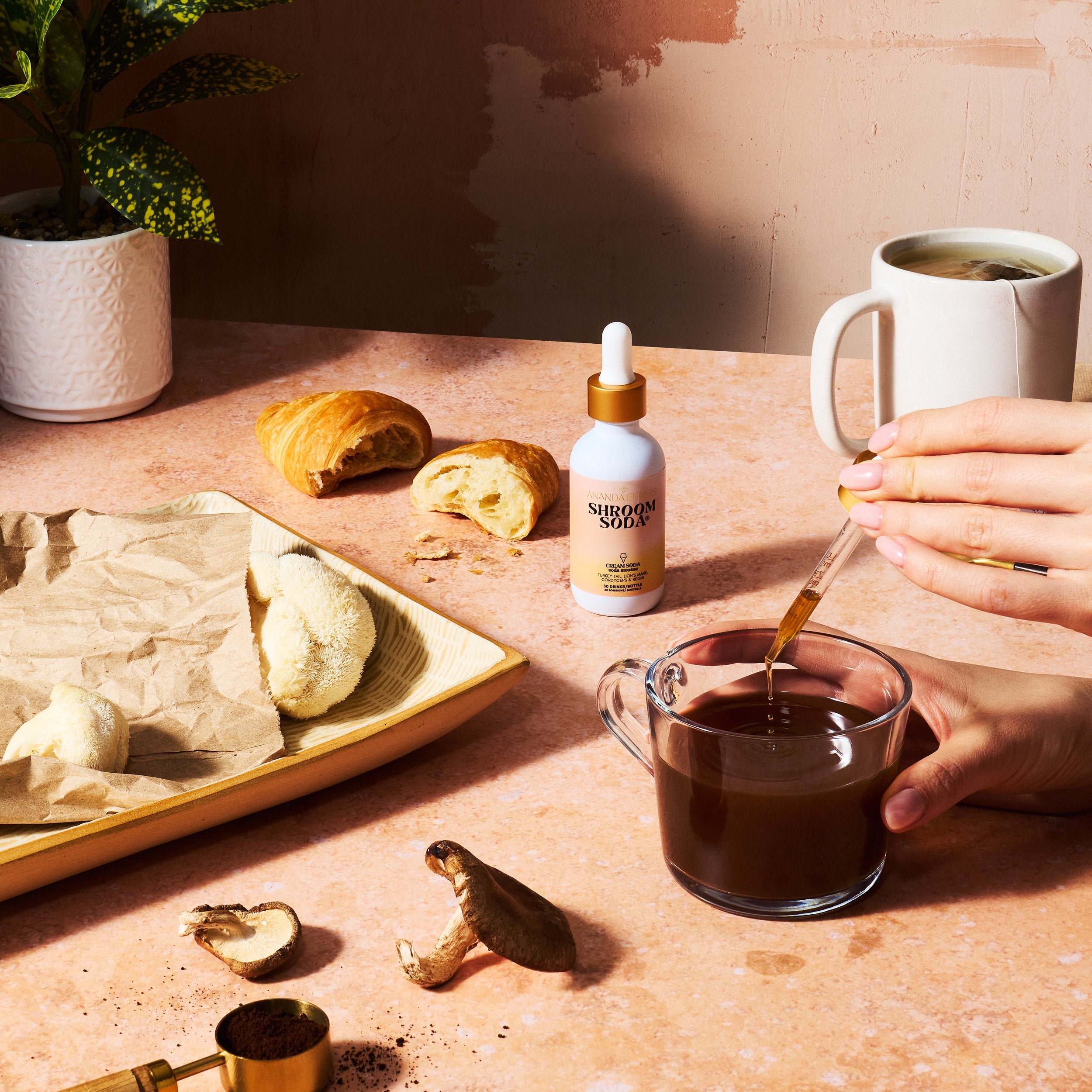 Person pouring Shroom Soda® from a dropper into a cup on a table 