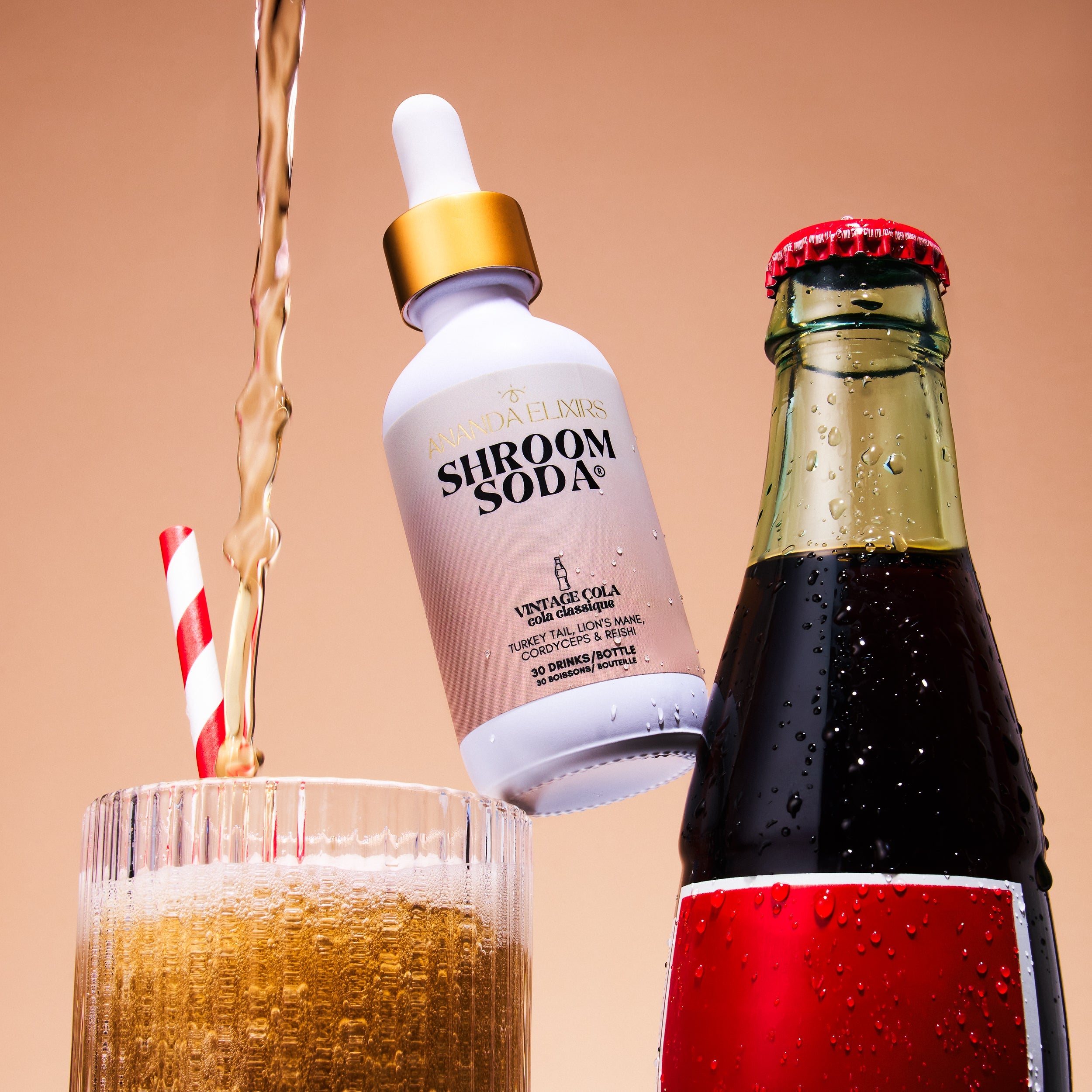 Shroom Soda bottle being poured into a glass with a red and white striped straw, next to a bottle of vintage cola.