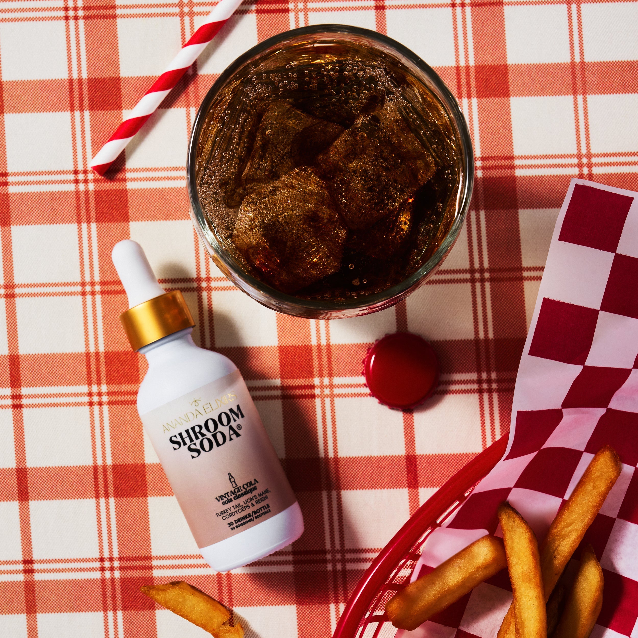 Shroom Soda bottle with a glass of soda and fries on a red and white checkered tablecloth.