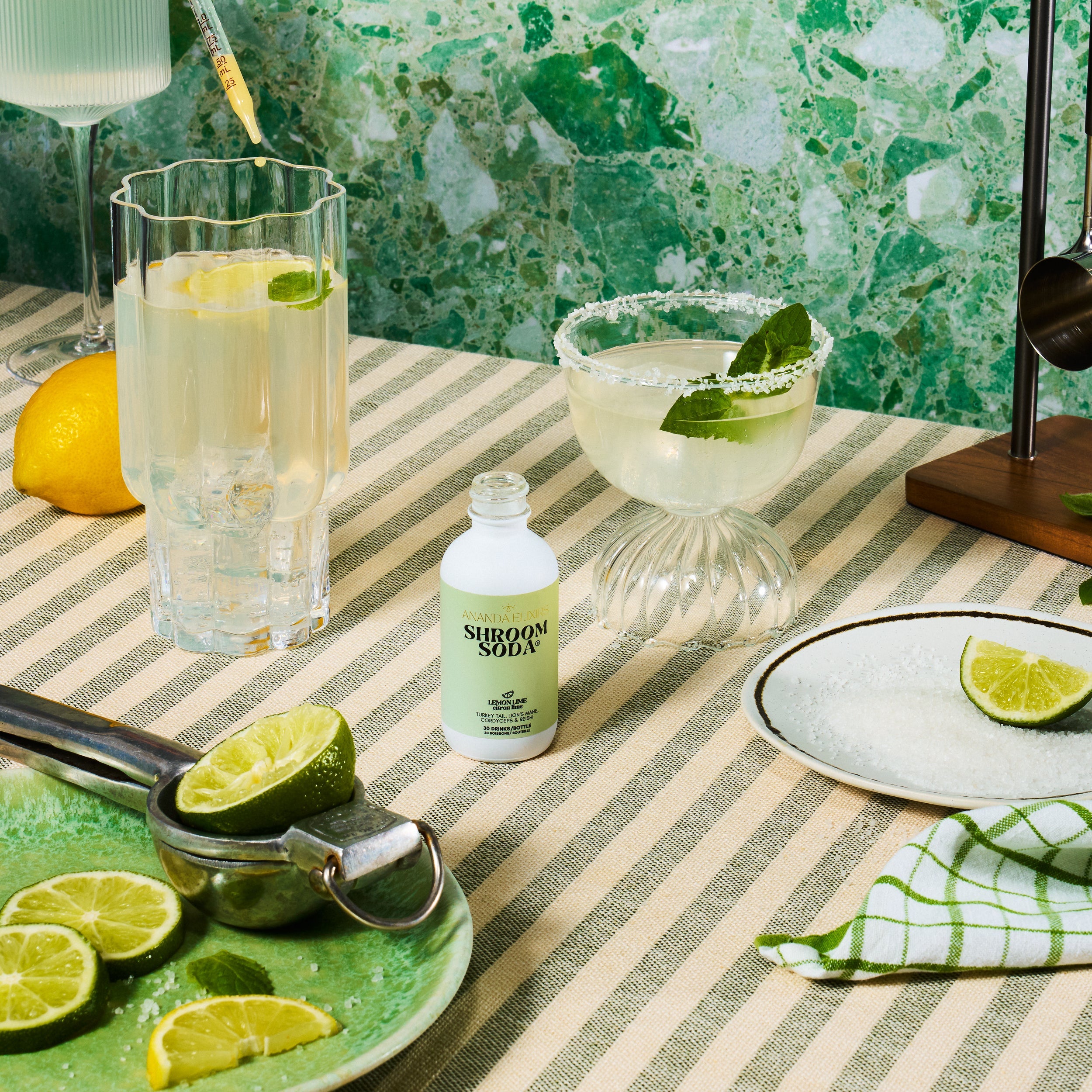 Table setting with a bottle of 'Shroom Soda', a glass of lemonade, and a margarita on a green and white striped tablecloth.