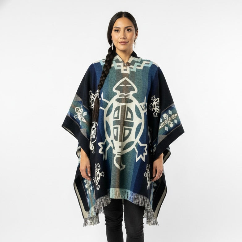 A woman modeling a dark blue and teal woven poncho with white and gray geometric turtle and tribal-style patterns, set against a plain light gray background.