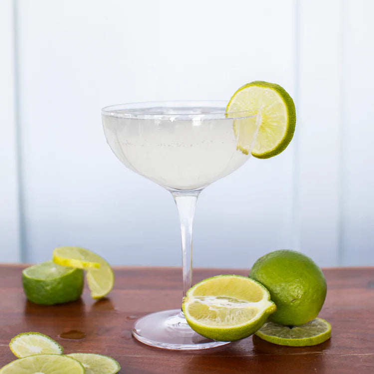 Cocktail in a martini glass with lime wedges on a wooden surface