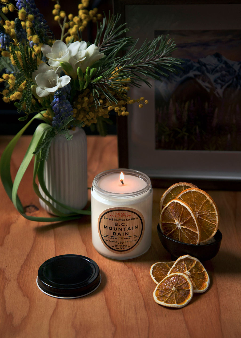 Candle with a label, dried oranges, and flowers on a wooden surface