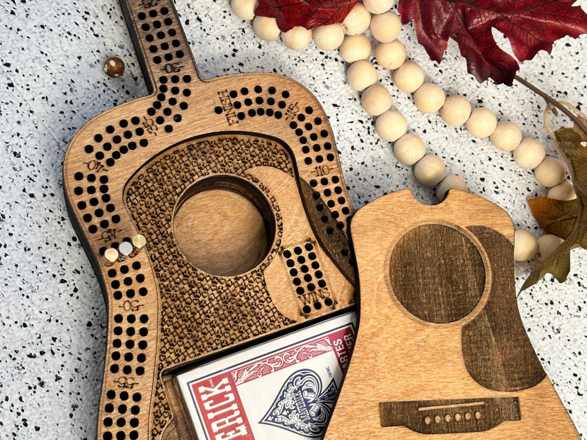 Wooden guitar-shaped cribbage board with card holder and beads on a textured surface.