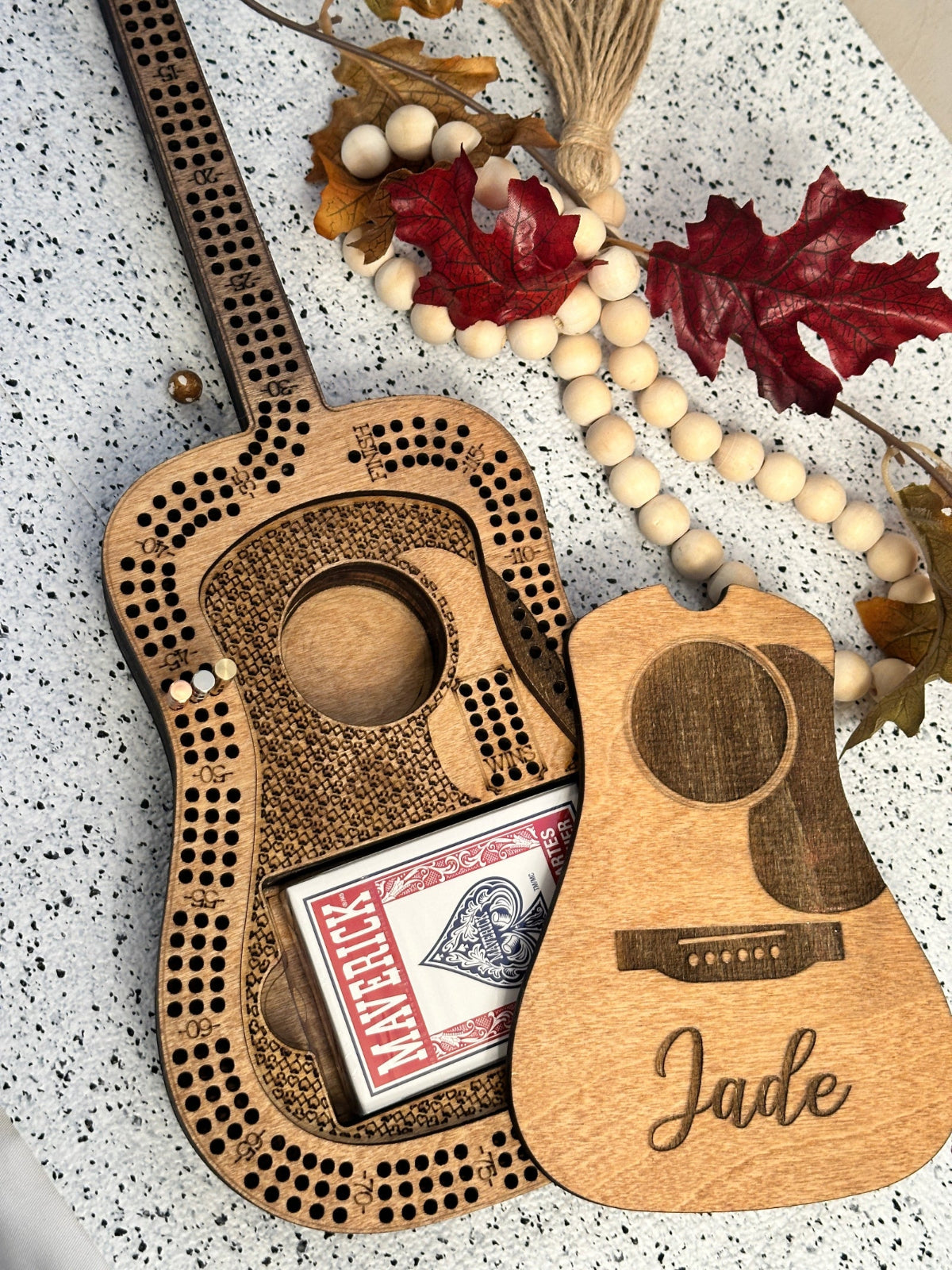 Wooden guitar-shaped cribbage board with card holder and beads on a textured surface.