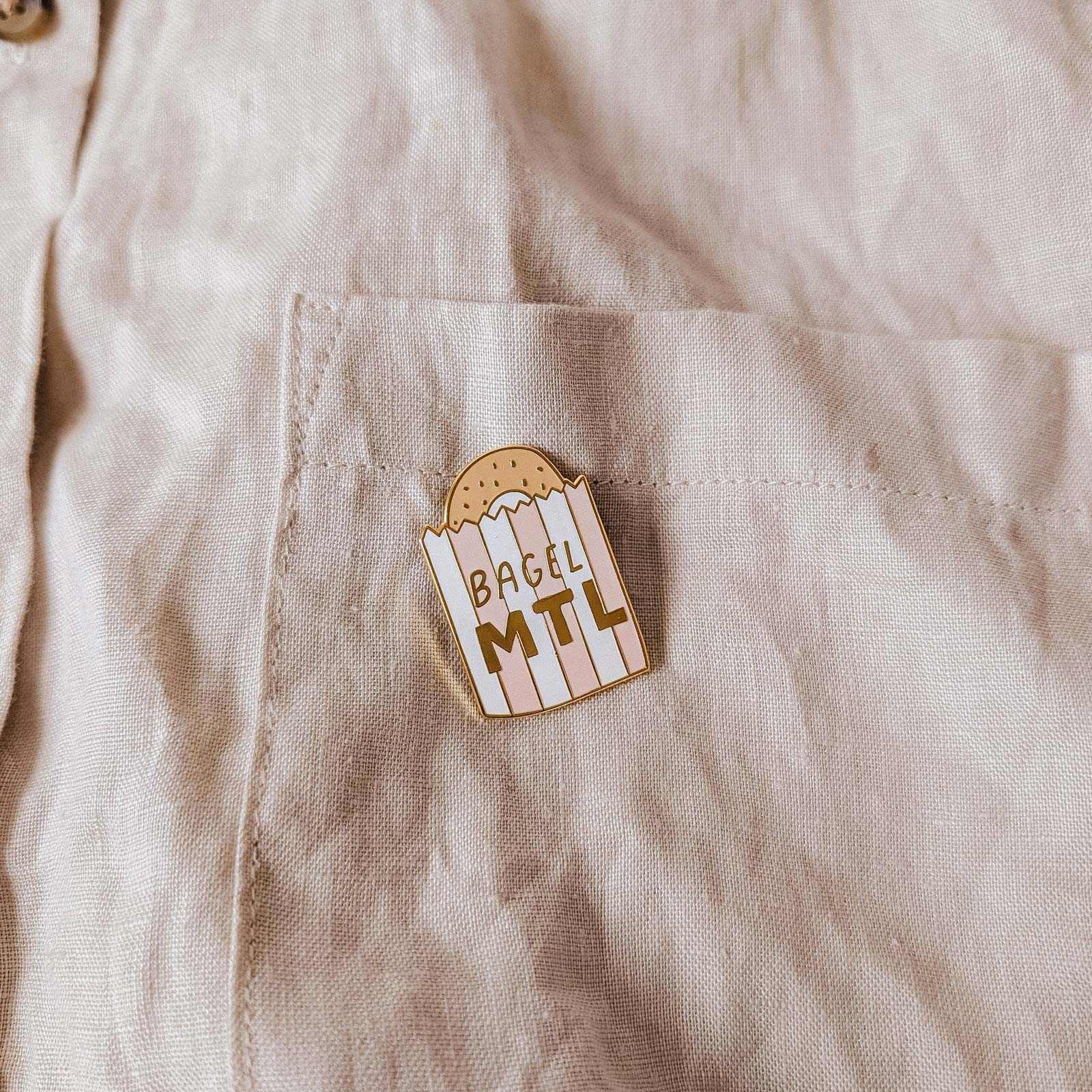mimi-and-august Pin with 'Bagel MTL' on a beige shirt