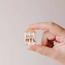 mimi-and-august Hand holding a bagel-shaped enamel pin with 'Bagel MTL' text on a plain background