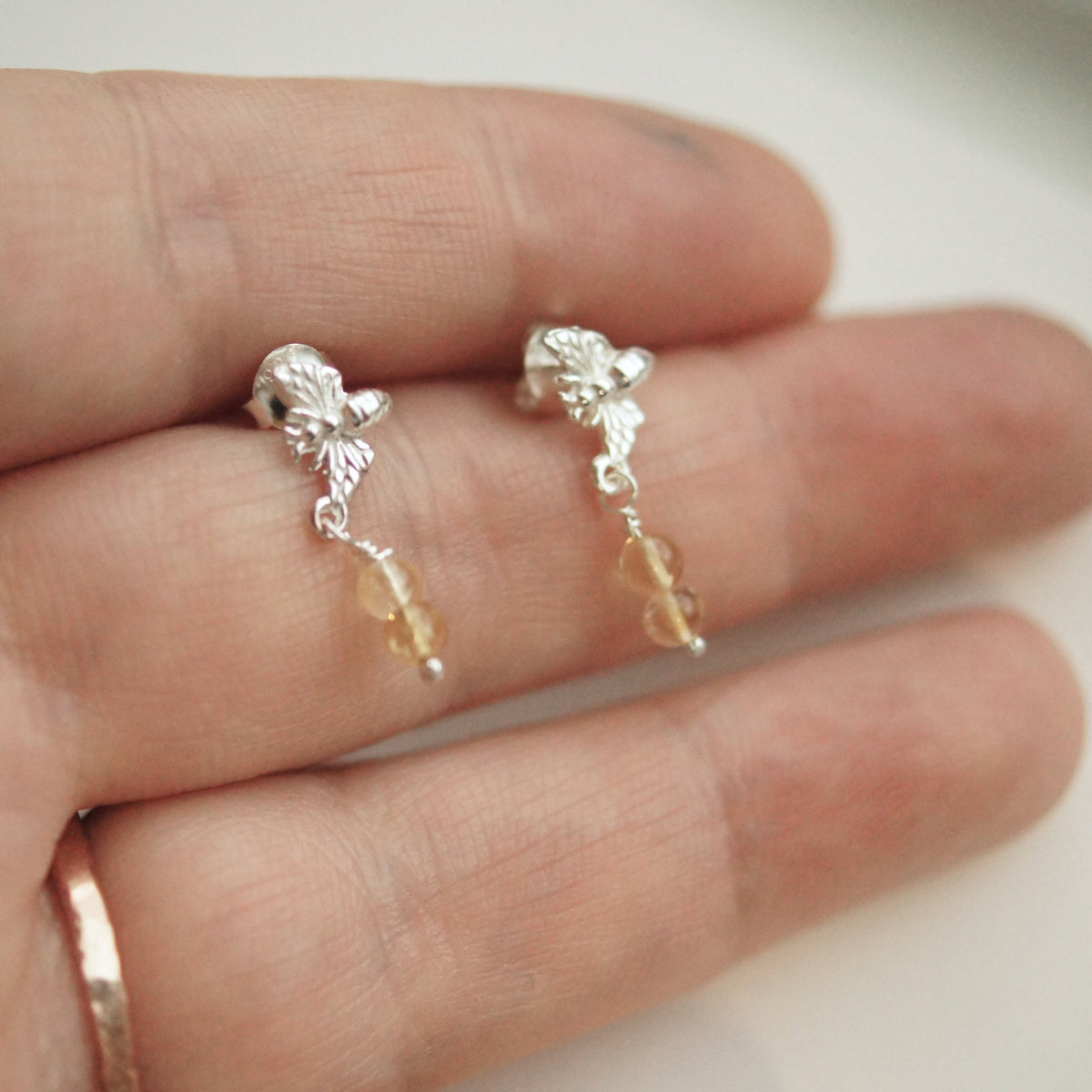 Silver earrings with dangling beads on a hand against a neutral background