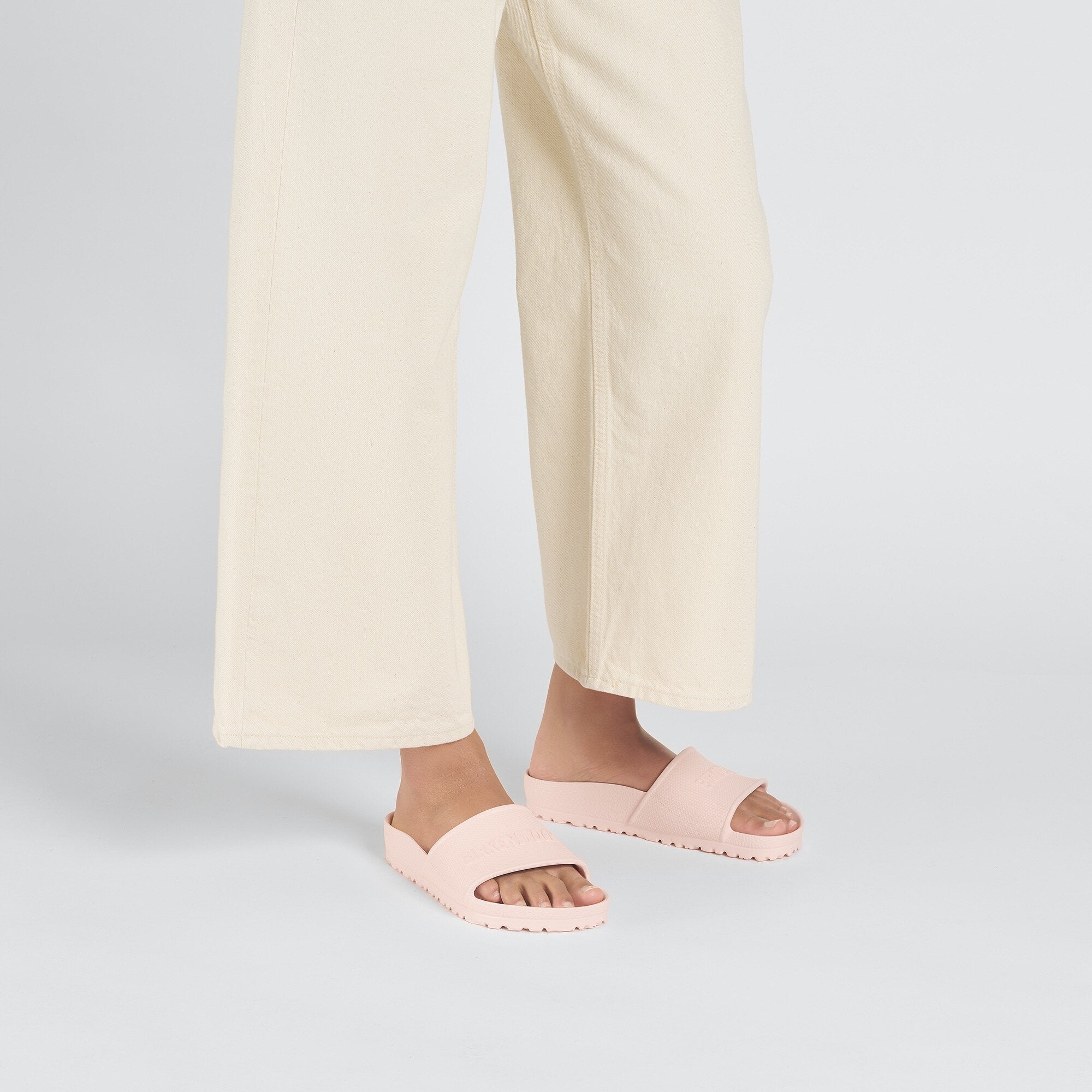 Person wearing Birkenstock Barbados EVA slides in light rose color with wide pants.