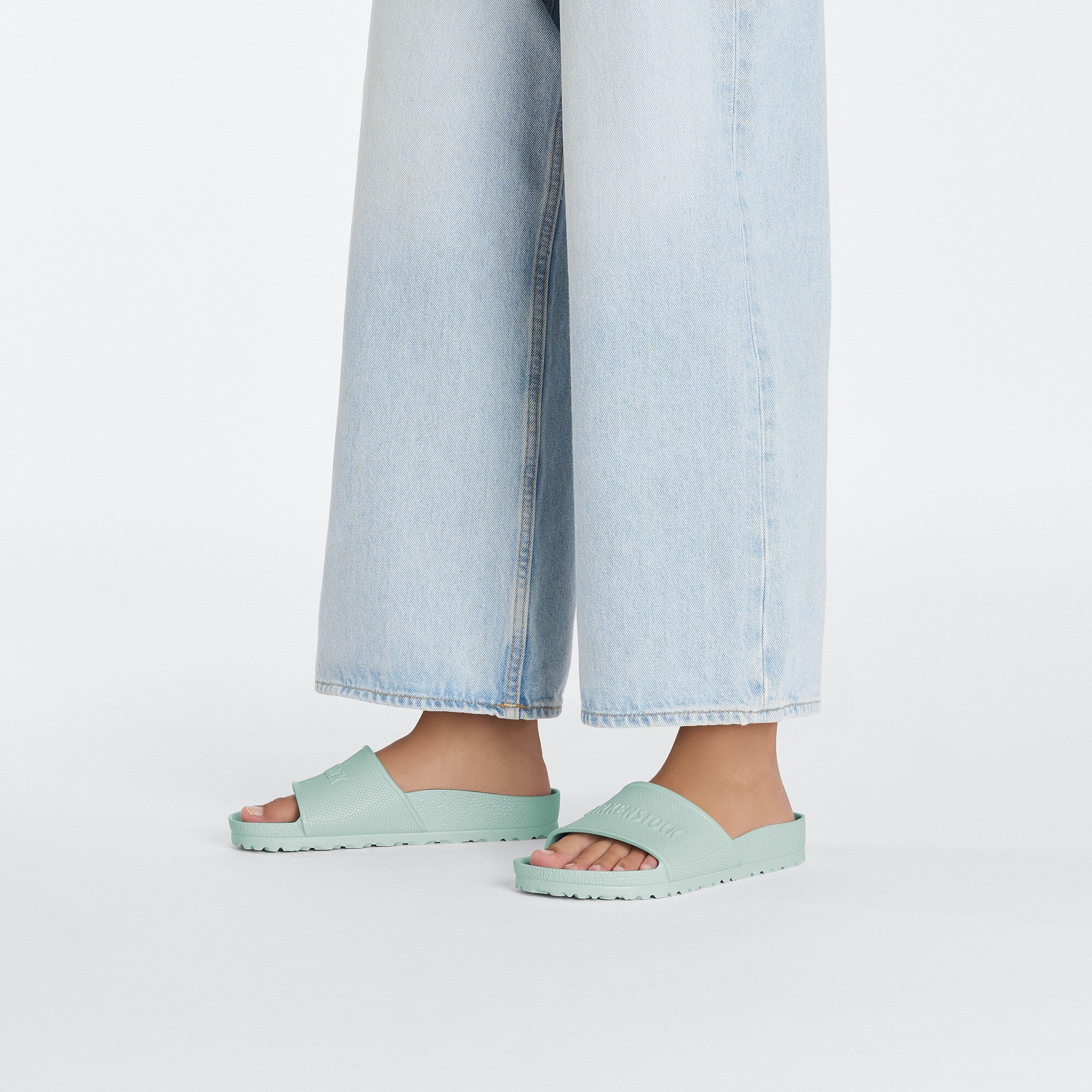 Birkenstock Barbados EVA slide in surf green, easy-to-wear summer footwear, paired with light blue wide-leg jeans.