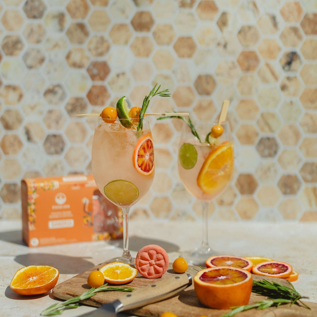 Two Poseidn cocktail flavors with fruit garnishes on a table with a tiled wall background