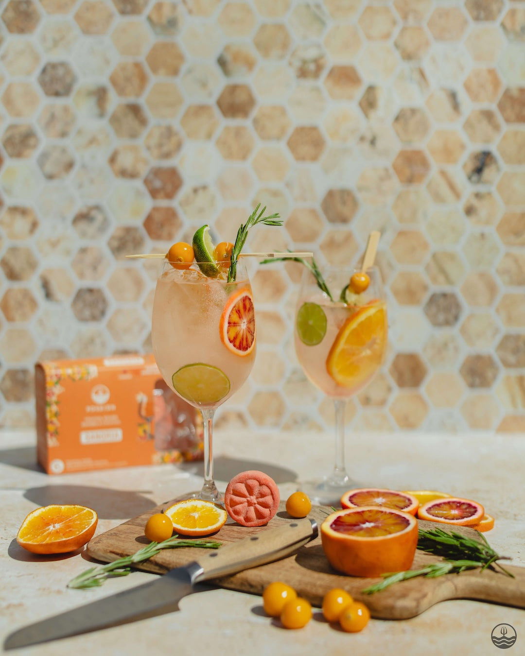 Two Poseidn cocktail flavors with fruit garnishes on a table with a tiled wall background