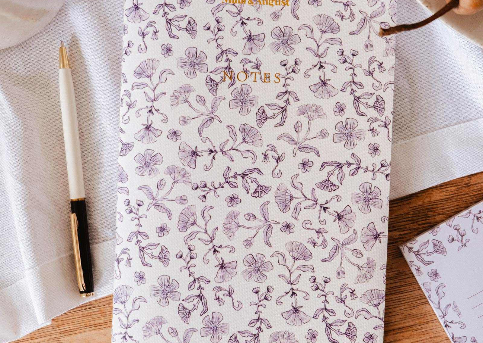 mimi-and-august Floral-patterned notebook on a wooden surface with a pen and decorative elements.