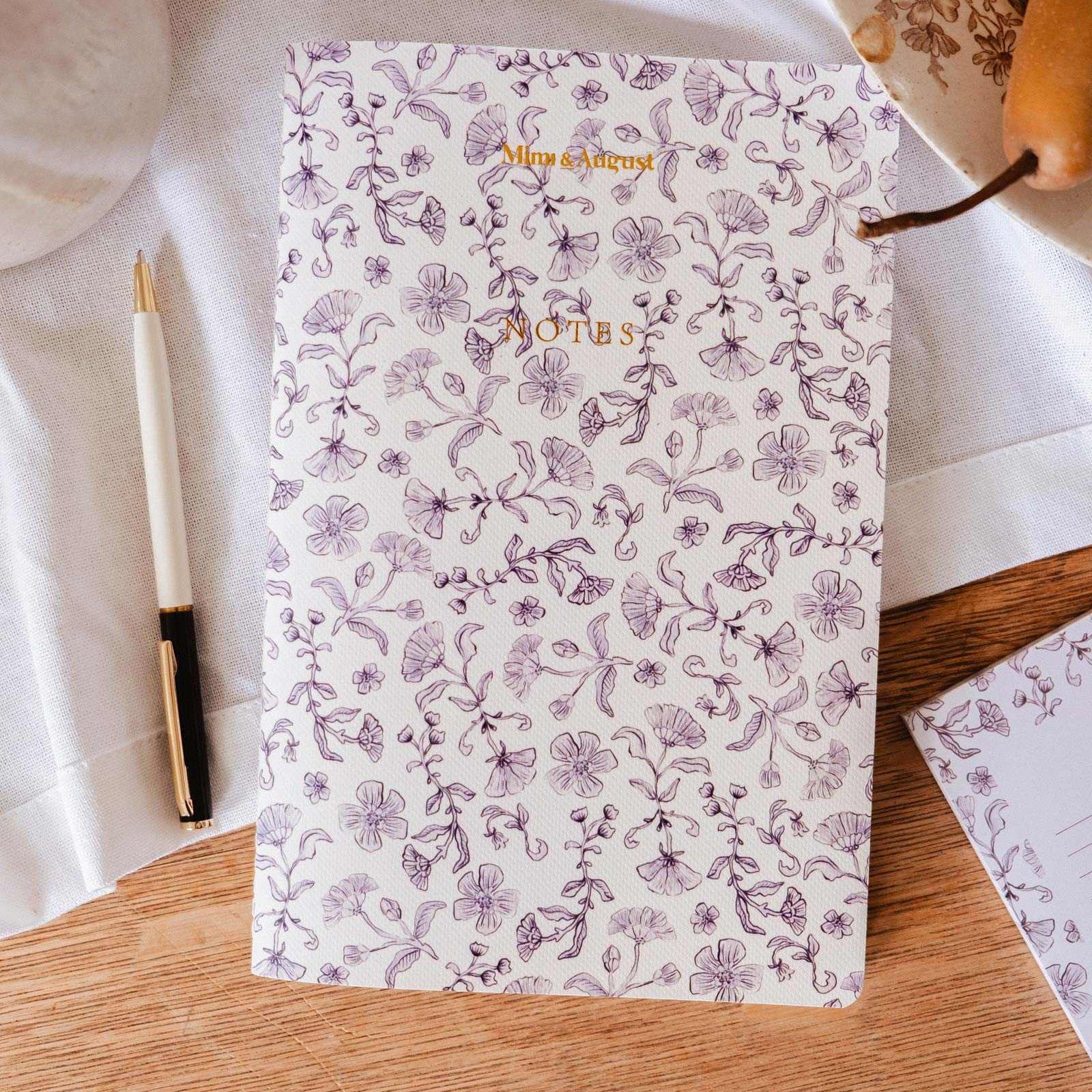 mimi-and-august Floral-patterned notebook on a wooden surface with a pen and decorative elements.
