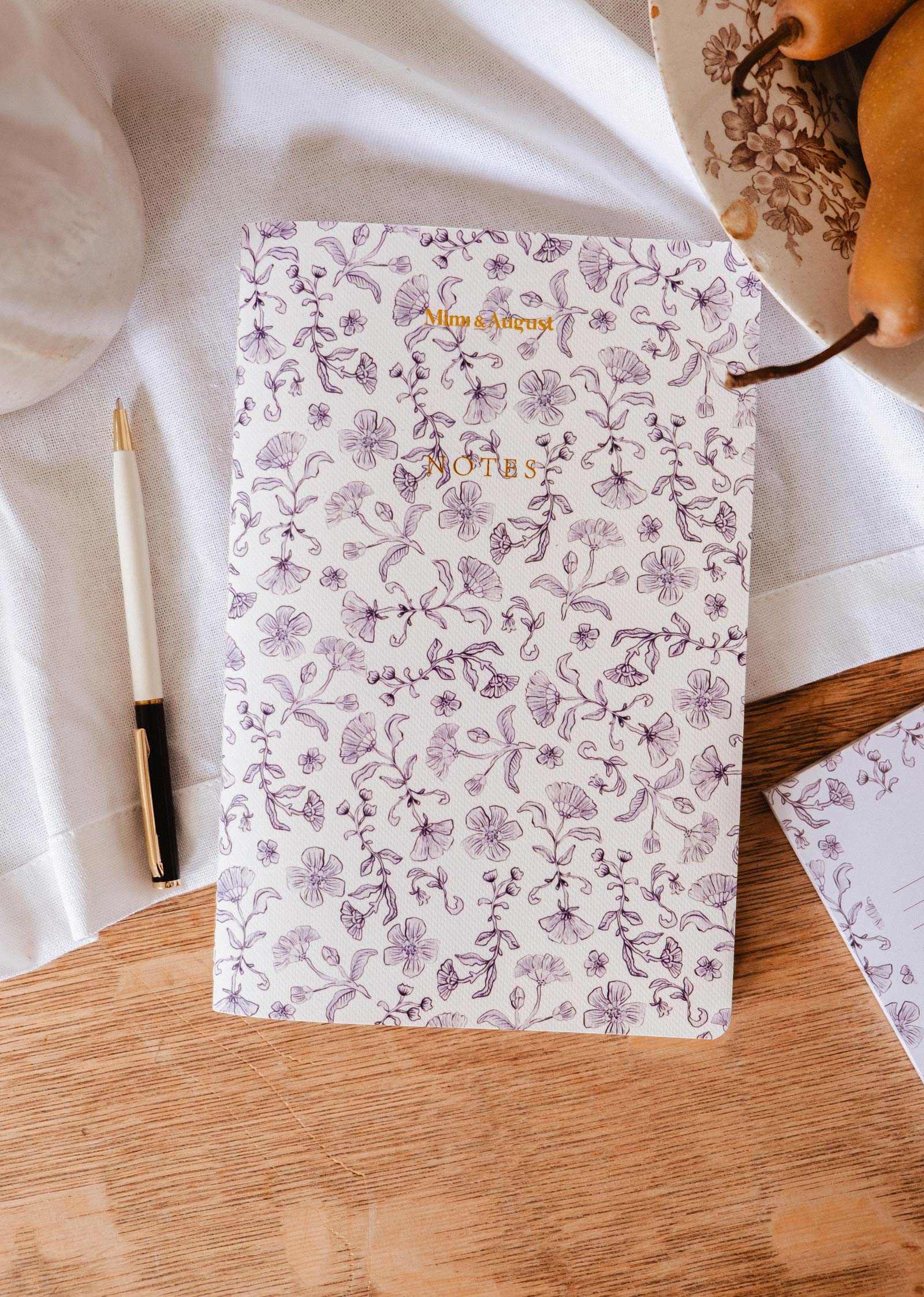 mimi-and-august Floral-patterned notebook on a wooden surface with a pen and decorative elements.