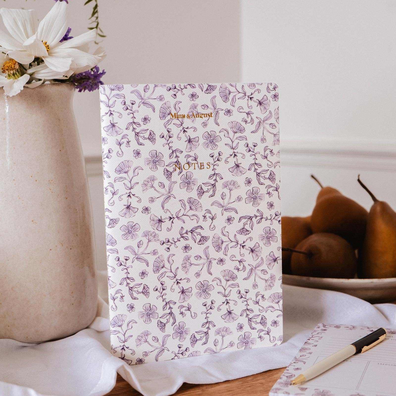mimi-and-august Floral-patterned notebook on a table with a vase of flowers and pears in the background