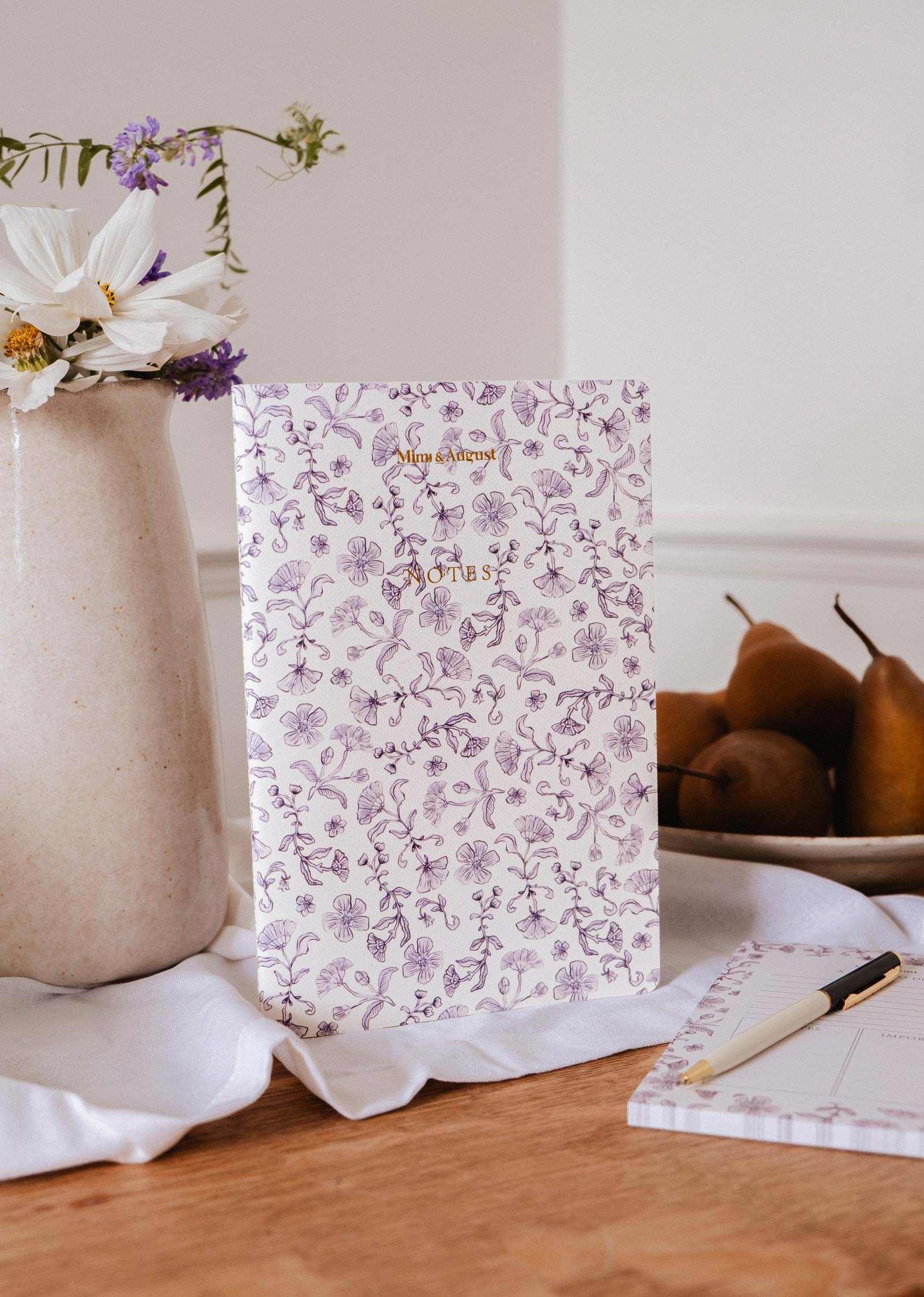 mimi-and-august Floral-patterned notebook on a table with a vase of flowers and pears in the background