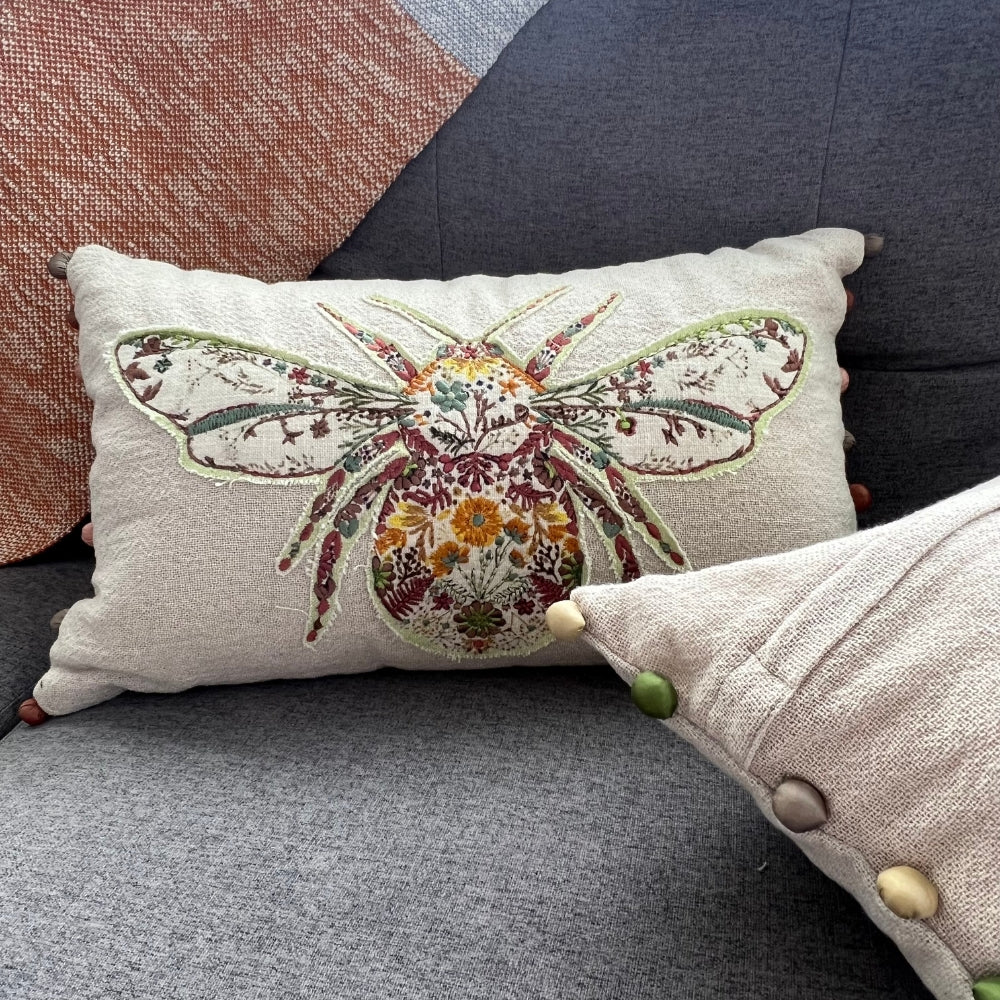 Decorative pillow with a floral bee design on a gray couch.
