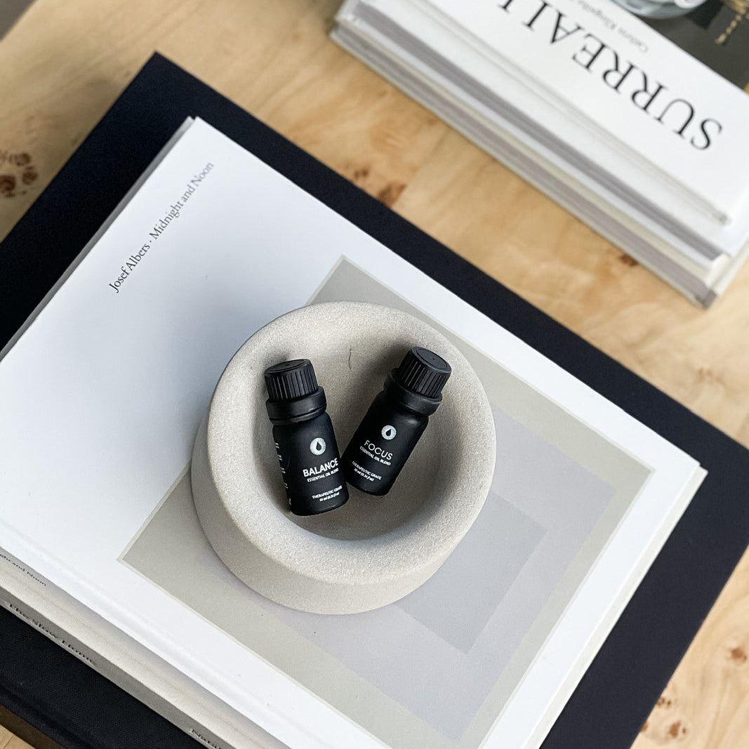 Two black bottles in a white bowl on a wooden surface with a book titled 'Surrealism' in the background.