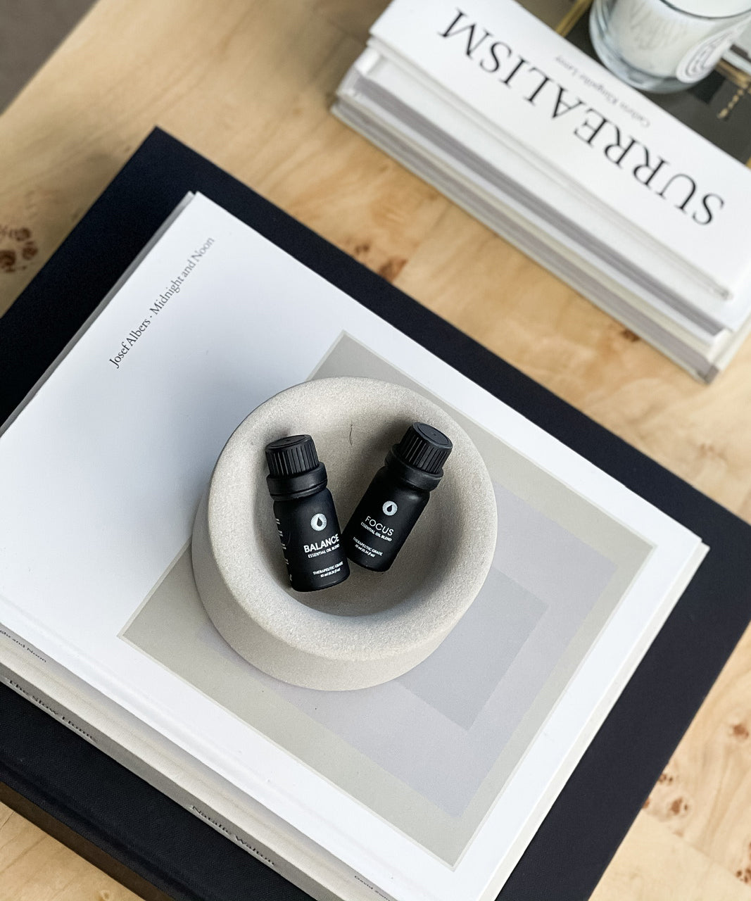 Two black bottles in a white bowl on a wooden surface with a book titled 'Surrealism' in the background.